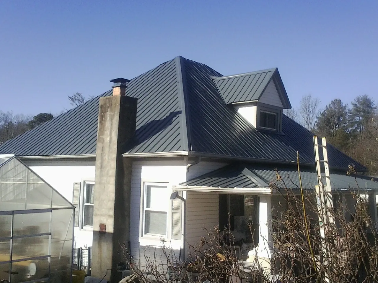 Dark blue standing seam metal roof on a white farmhouse with dormer — Slate & Tile Roof Repair by Roofing Brothers in Constableville
