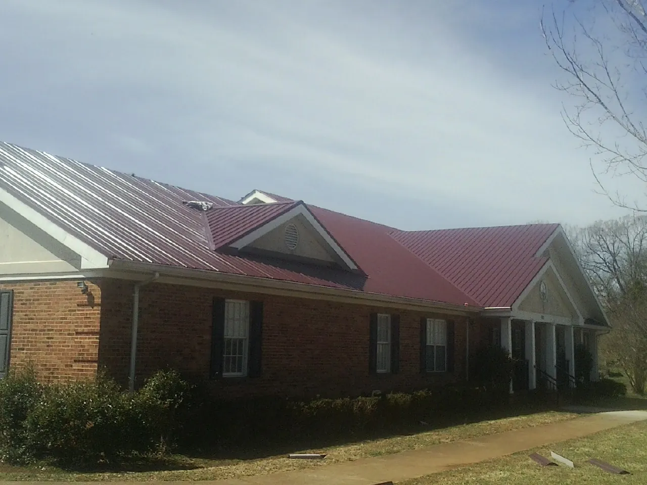 Red metal roof with gabled entries on a long brick building, from a Hail Damage Roof Repair job in Constableville