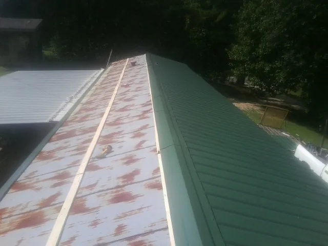 Old rusted panels beside newly installed green metal roofing — Wind Damage Roof Repair by Roofing Brothers in Constableville