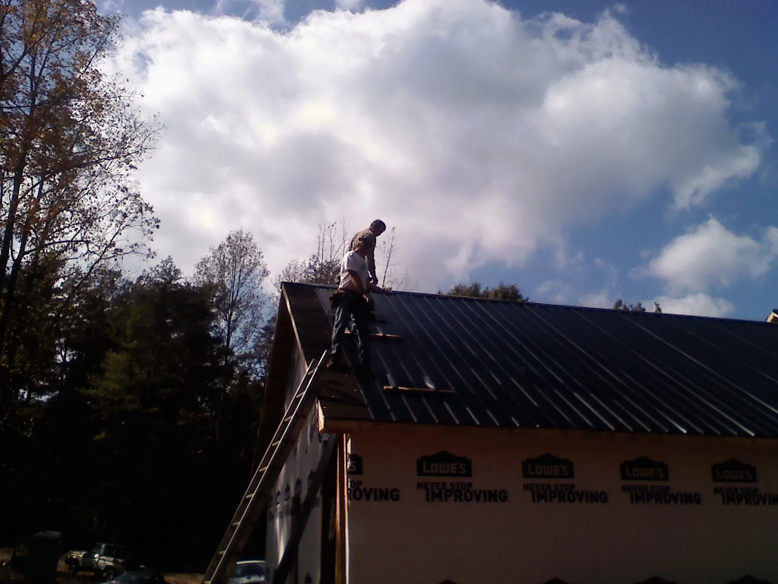 Roofer fastening dark metal panels high against a cloudy sky, from a Roof Inspection job in Constableville
