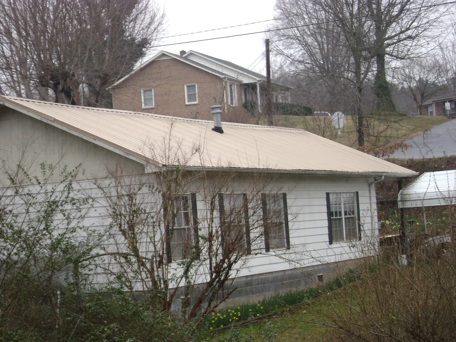 Tan metal roof on a white sided house set into a hillside — Commercial Roofing by Roofing Brothers in Constableville