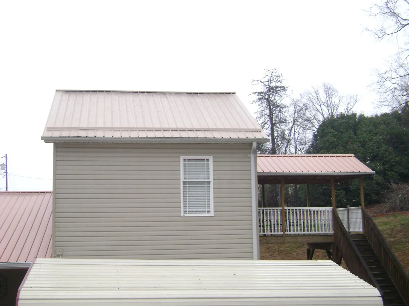 Tan metal roofs on a two story addition and attached porch, from a Roof Replacement job in Constableville